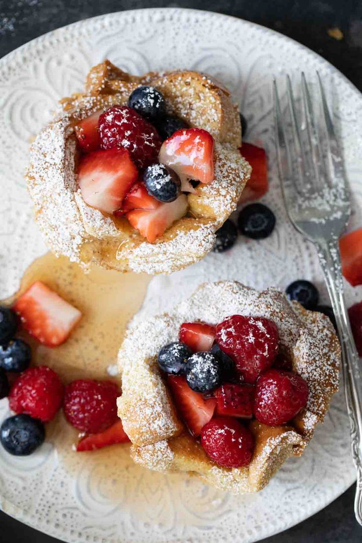 two pastries with berries and powdered sugar on a plate next to a fork