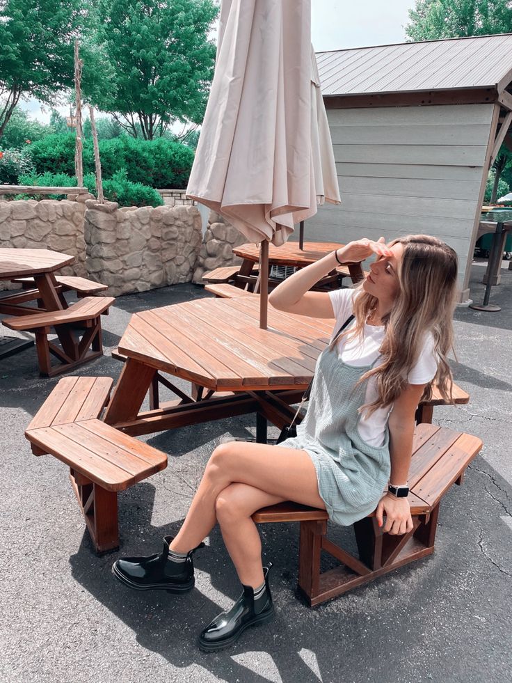 a woman sitting on top of a wooden bench next to an umbrella over her head