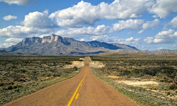 an empty road in the middle of nowhere with mountains in the background