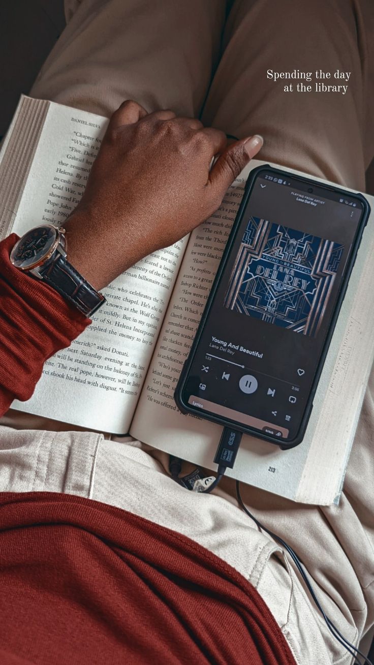 a person laying down reading a book with an electronic device on their lap next to them