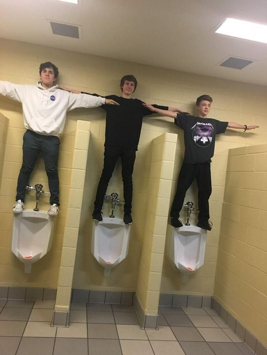 three young men standing on urinals in a bathroom with their arms spread out