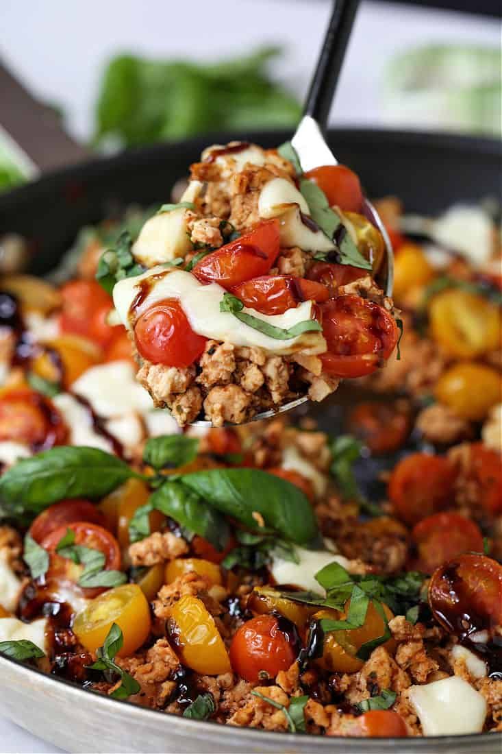 a spoon full of meat and vegetables being lifted from a skillet with basil leaves