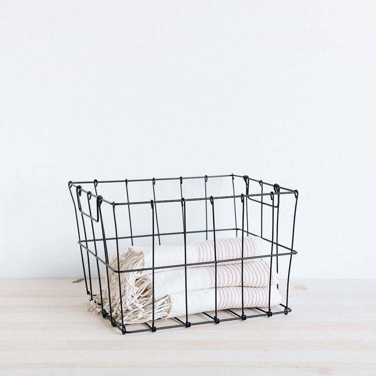 a black wire basket with folded towels in it on a wooden table next to a white wall