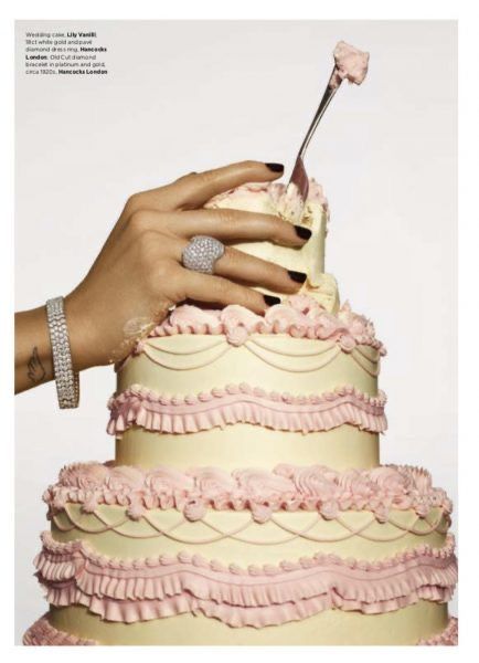 a woman's hand holding a spoon over a layered cake with pink icing and ruffles