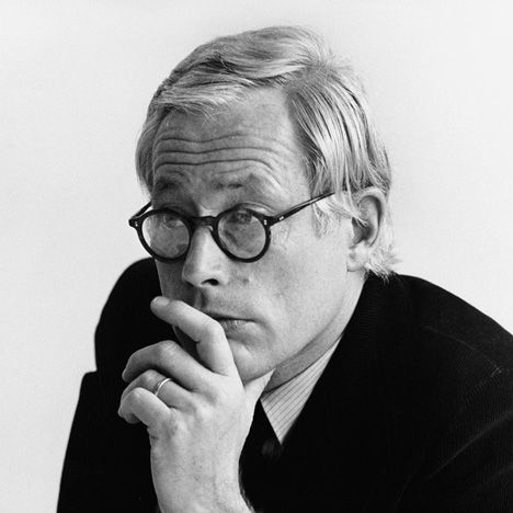 black and white photo of a man with glasses looking at the camera while leaning his chin on his hand