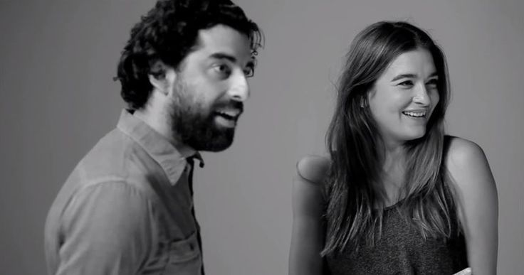 a man standing next to a woman in front of a white wall and talking on the phone