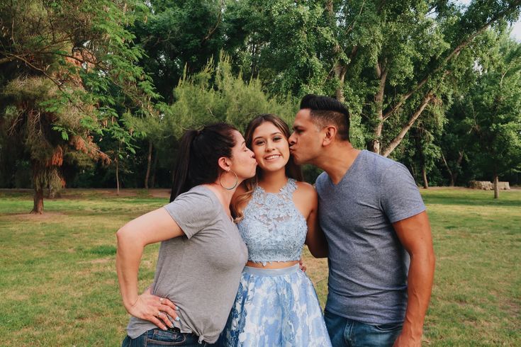 three people are posing for a picture in the grass with one woman kissing the other man's cheek