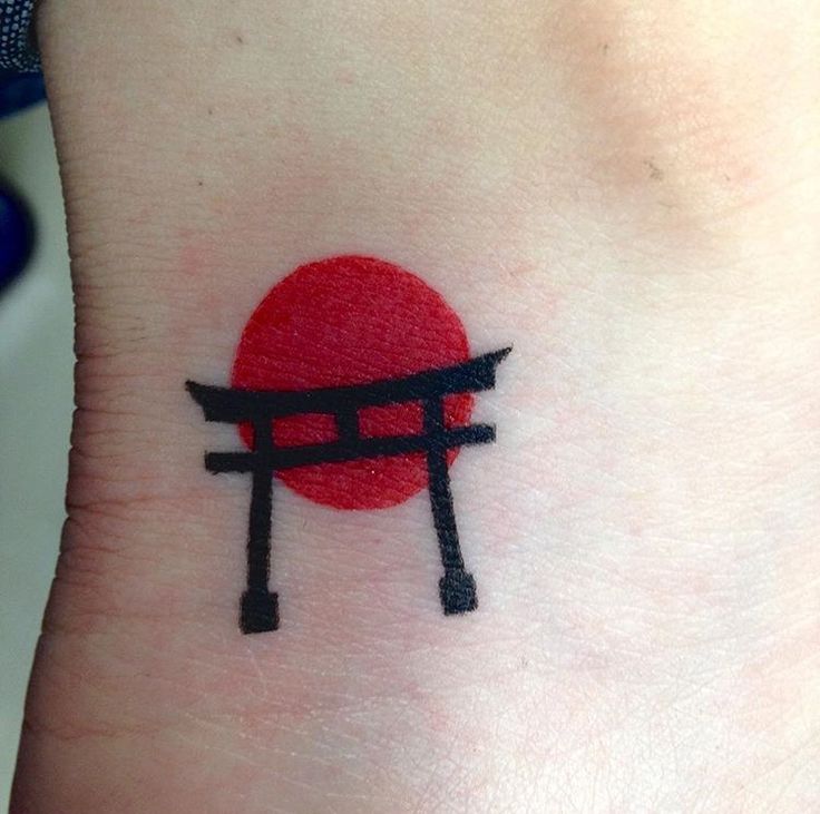 a small tattoo on the wrist of a person with a red sun in the background