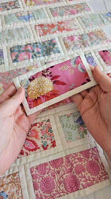 two hands are working on a patchwork quilt with pink and green flowers in the center