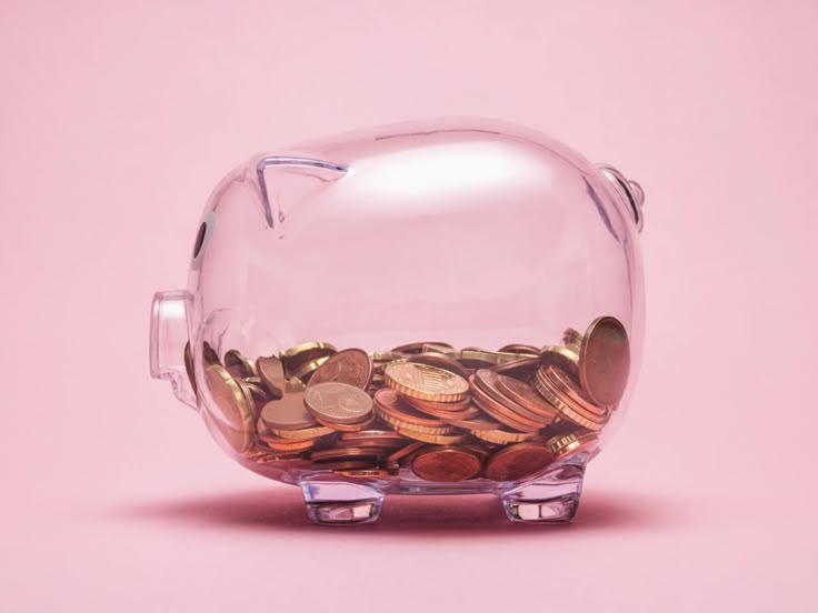 a glass piggy bank filled with coins on a pink background and the bottom half is empty