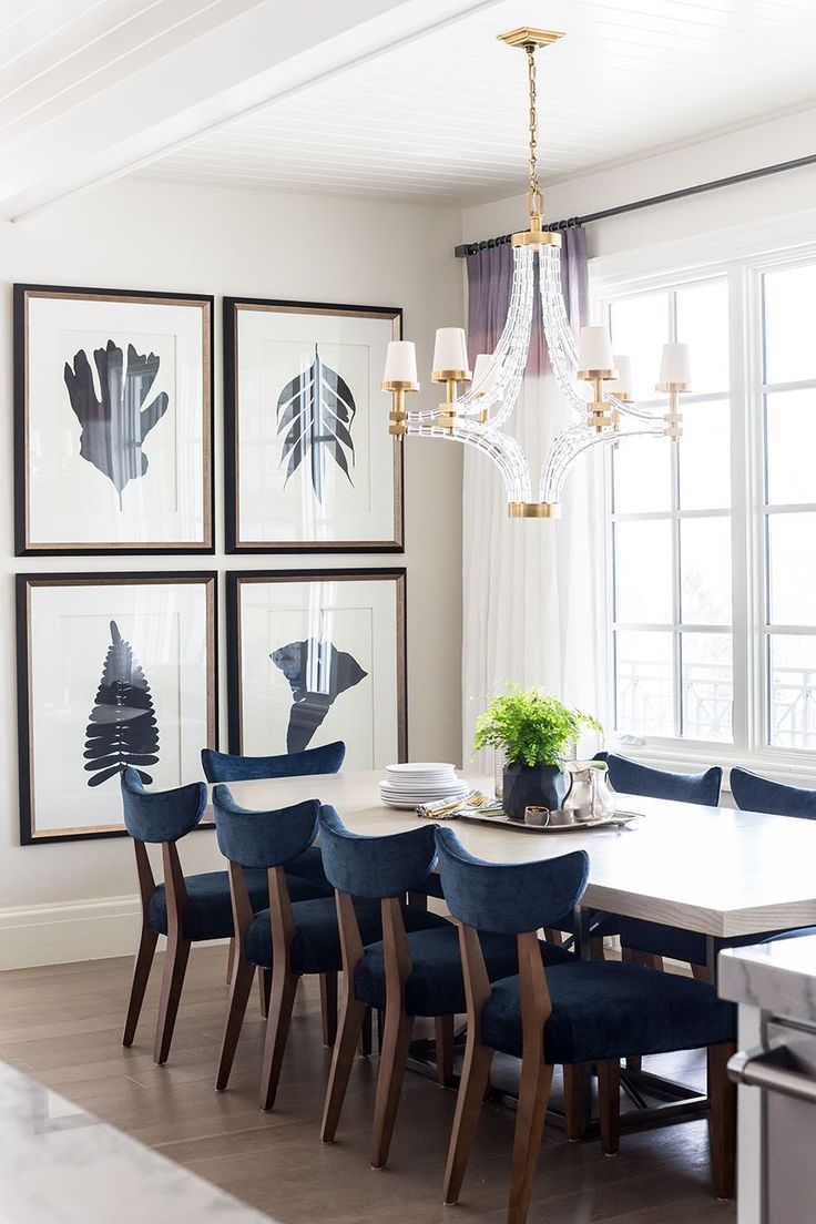 a dining room table with blue chairs and pictures on the wall above it in front of a chandelier