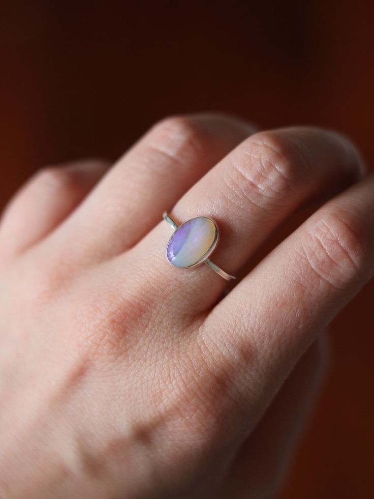 This dainty and extremely delicate ring features a beautiful Australian Lightning Ridge opal, set in a fine silver bezel with open back. The band is made with a sterling silver square wire. Size 6Handmade It's a perfect everyday ring - simple, yet full of character. Can be stacked and combined with other rings or worn by itself, for a more minimalist look. Delicate purples make each opal absolutely unique, with its own stunning colours and inclusions. The look of the gemstone changes in differen Minimalist Oval Opal Ring Gift, Minimalist Opal Rings For Gifts, Minimalist Opal Rings For Gift, Handmade Minimalist Opal Ring For Anniversary, Minimalist Handmade Opal Ring For Anniversary, Oval Opal Stackable Rings As Gift, Minimalist Handmade Opal Promise Ring, Delicate Sterling Silver Opal Ring For Anniversary, Minimalist Opal Ring As A Gift