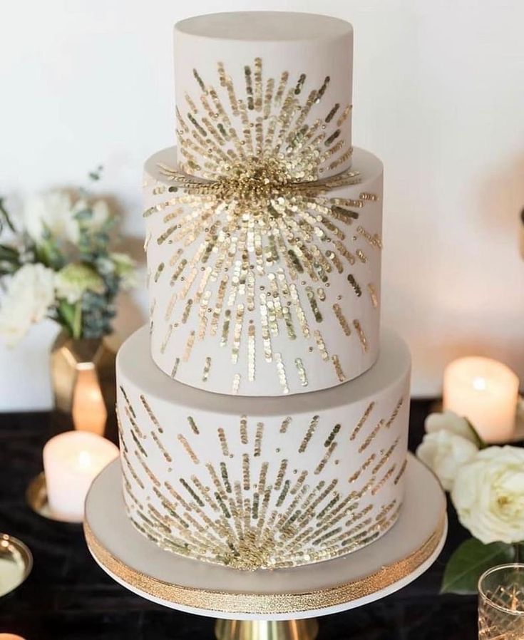 a three tiered wedding cake with gold sparkles on top and white flowers in the background