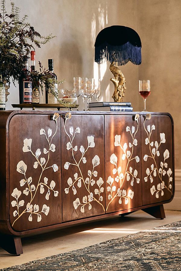 a sideboard with flowers painted on it next to a vase and wine glass holder