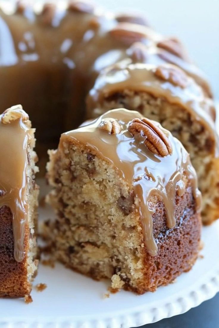 a bundt cake with frosting and pecans is cut in half on a white plate