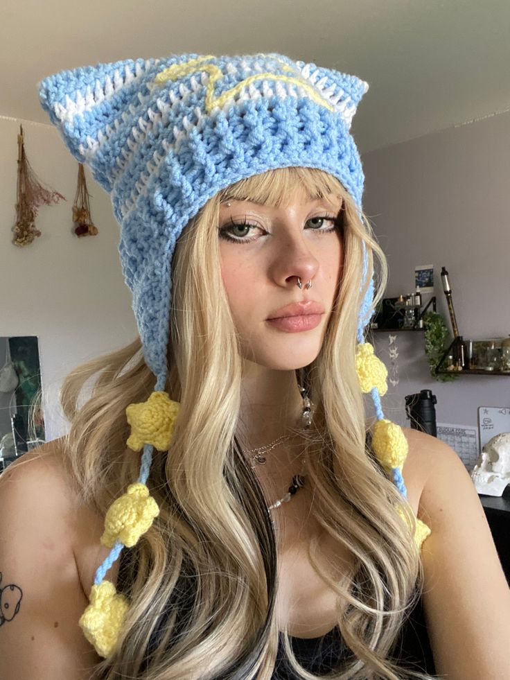 a woman with long blonde hair wearing a blue and yellow crochet cat hat