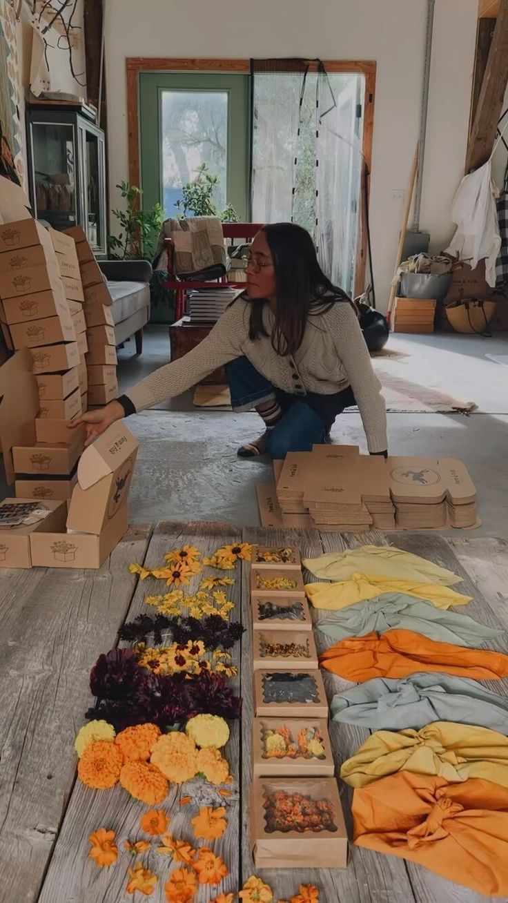 a woman sitting on the floor surrounded by boxes full of flowers and other items that have been placed in them