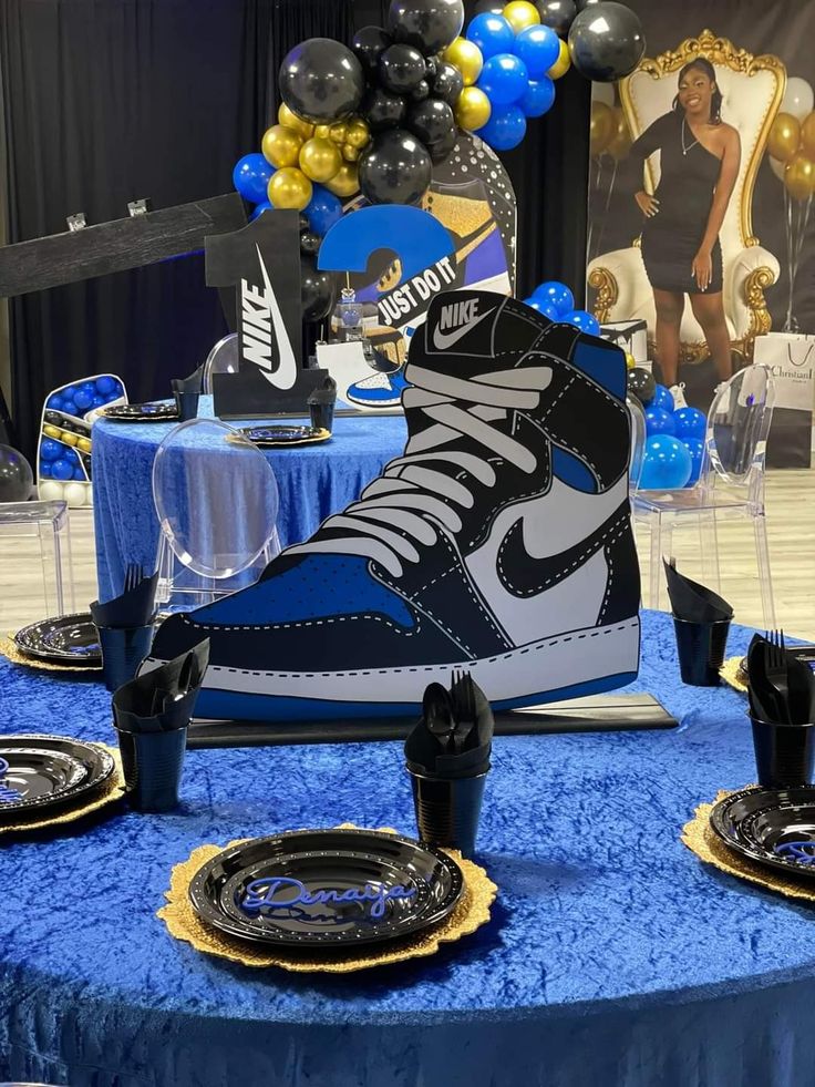 a blue table topped with black and white nike sneakers next to plates and cups on top of it