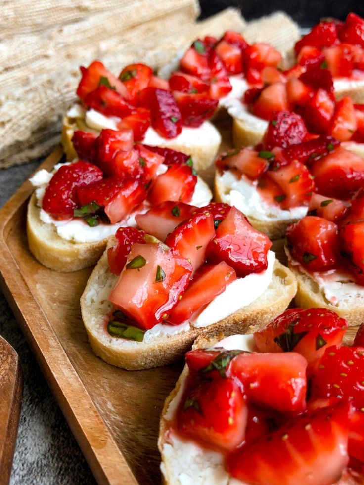 strawberries and cream cheese on toasted bread are arranged on a wooden cutting board