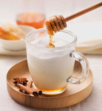 a glass mug filled with liquid and honey on a wooden plate next to cinnamons