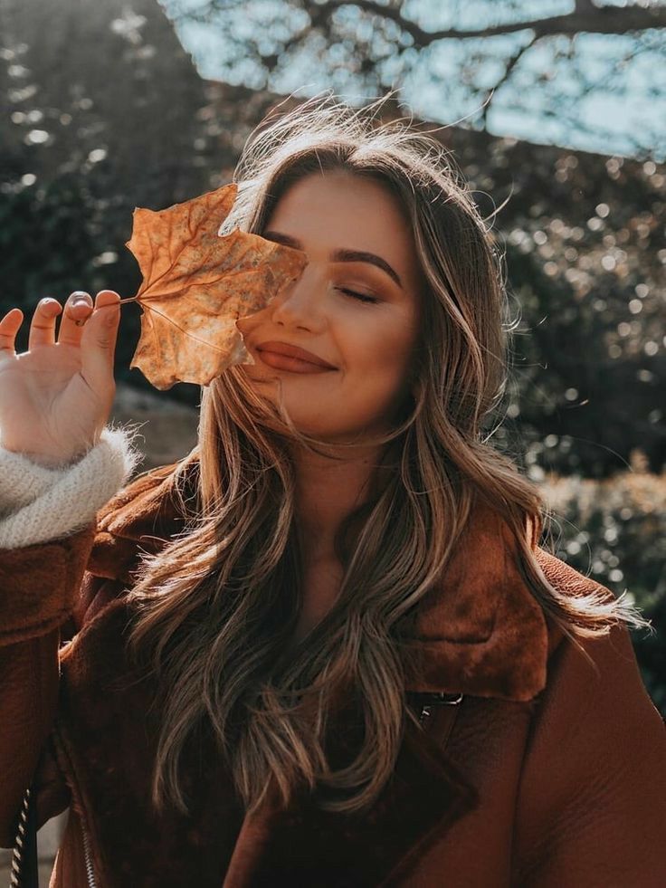 a woman holding an orange leaf in front of her face