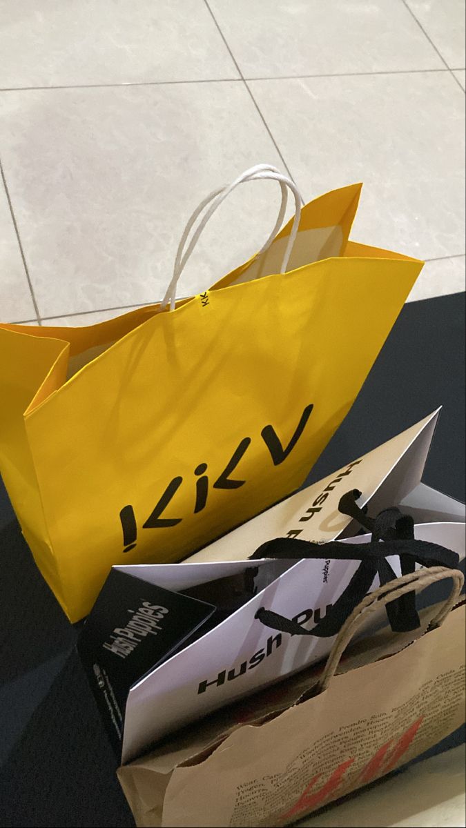 two shopping bags sitting on top of a table next to each other, one yellow and the other black