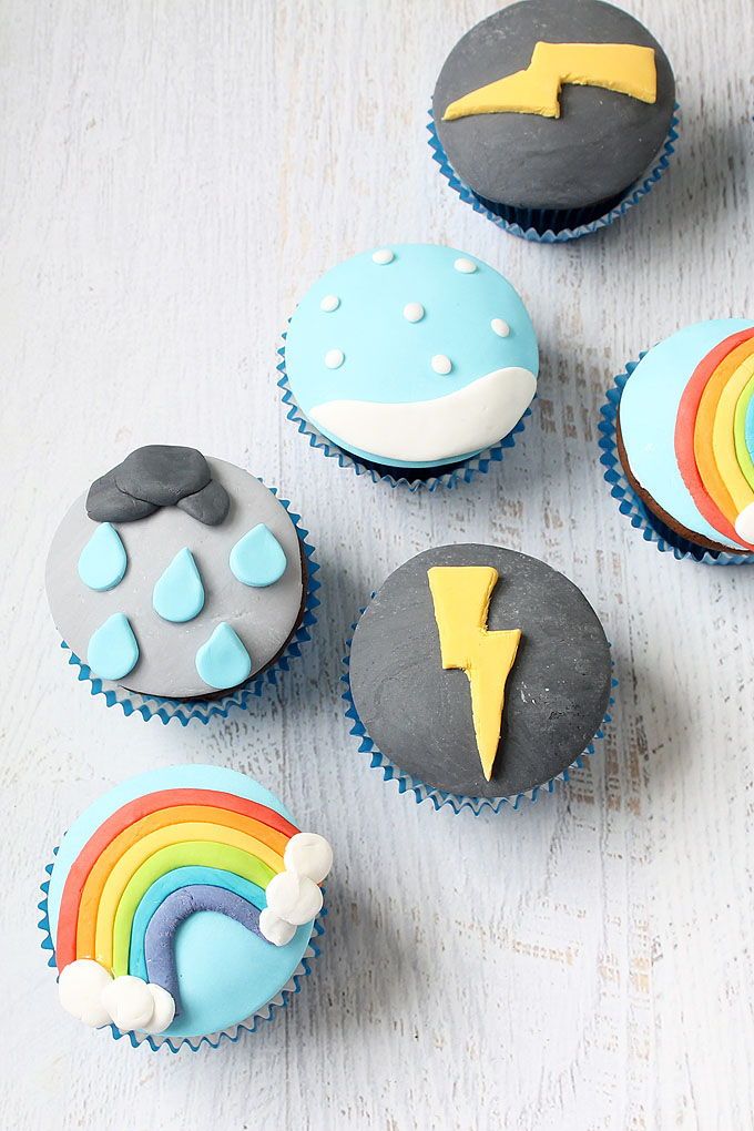 cupcakes with icing and rainbow designs on them sitting on a white table