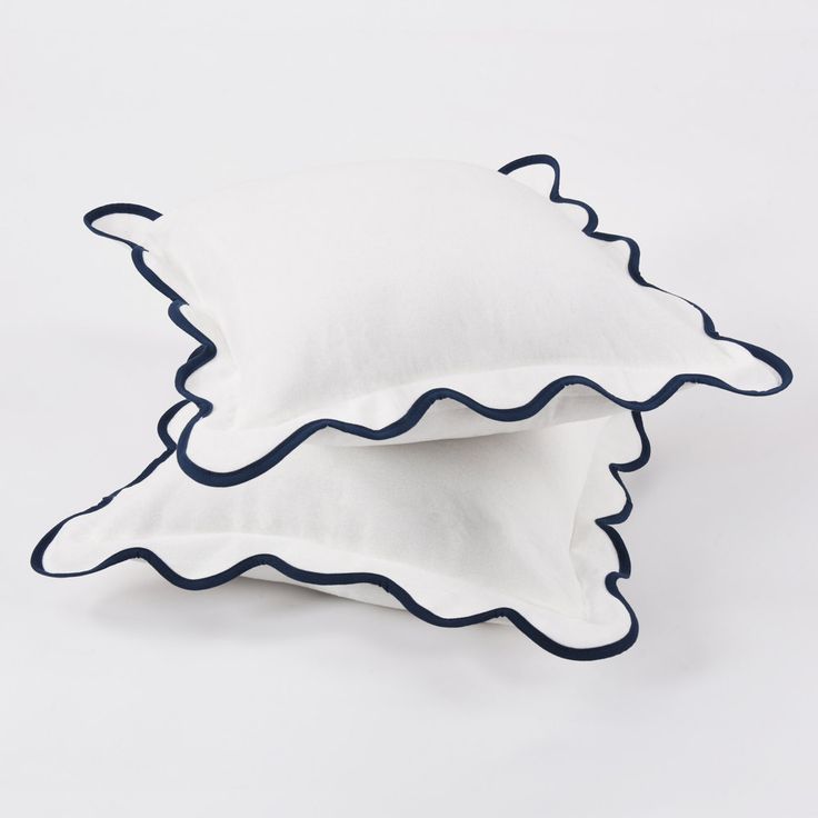 two pillows with scalloped edges are sitting on a white surface, one is blue and the other is white