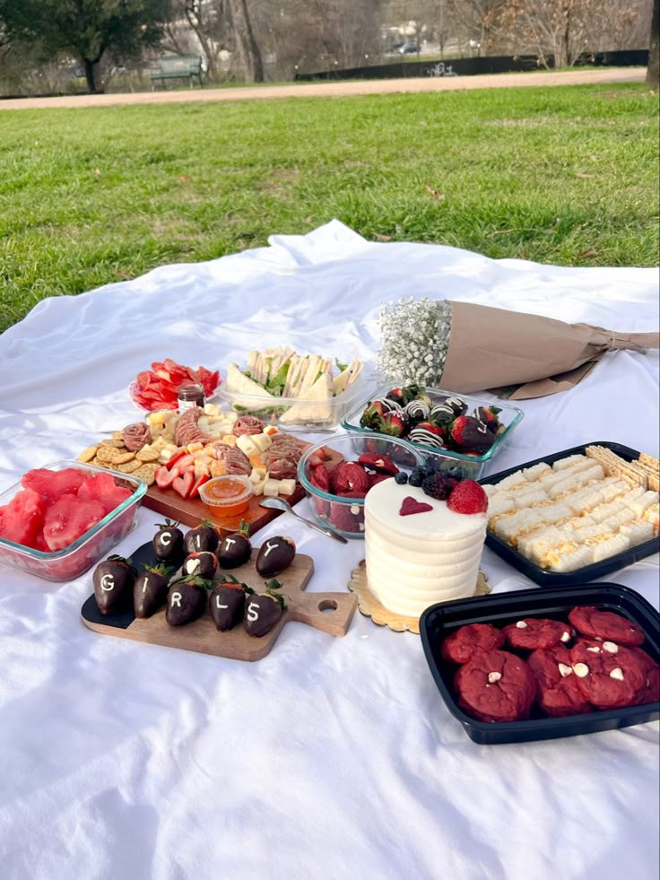 an outdoor picnic with desserts and fruit on the table in front of grass area