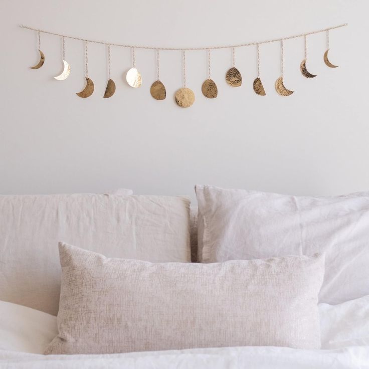 a white bed topped with lots of pillows next to a string of gold moon phases