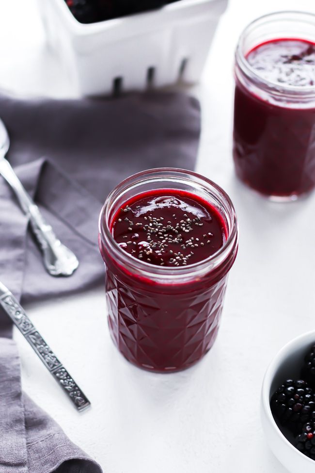 two jars filled with berries sit on a table next to spoons and silverware