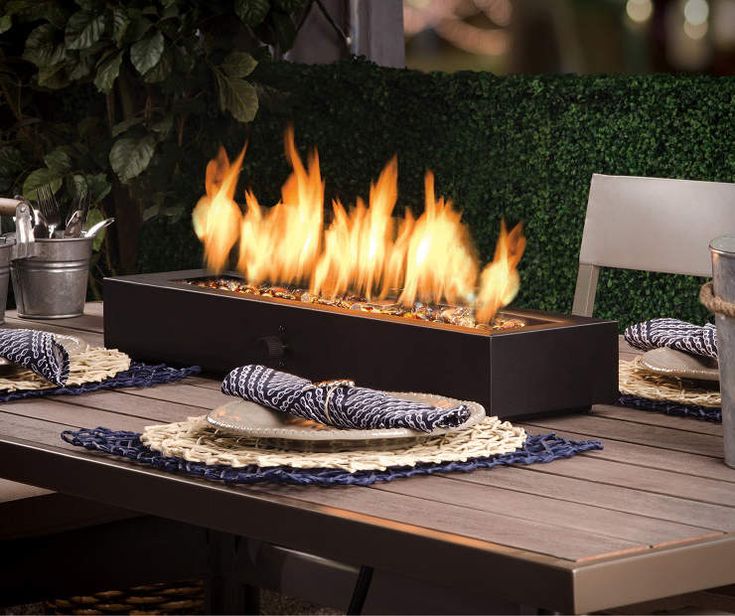 an outdoor table set with place settings and fire burning in the backround area