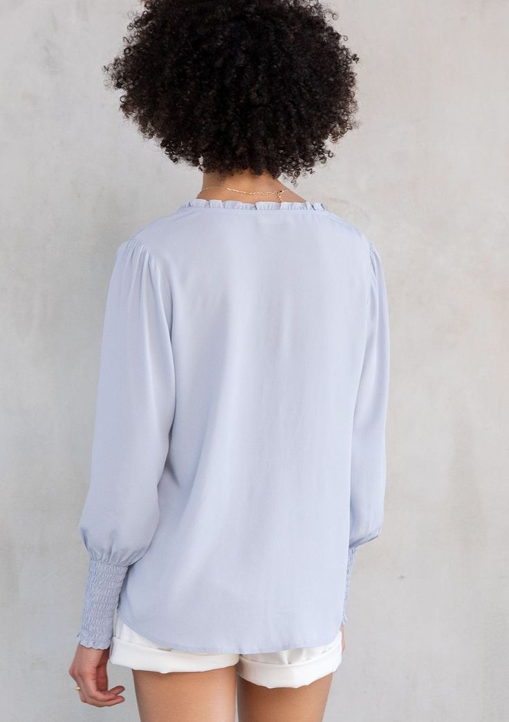 Designed in ultra-soft and silky crepe, this effortless bohemian peasant top is an instant classic. Featuring a delicate self-covered button front detail, voluminous long sleeves with a smocked elastic wrist cuff, and smocking along the shoulder. Try this versatile style tucked into trousers or untucked over jeans. Silky crepe Relaxed fit Long voluminous sleeve Smocked elastic wrist cuff Split v-neckline with ties Ruffled neckline Self-covered button front Smocked shoulder details Bohemian resor Billowy Long Sleeve Top With Smocked Cuffs, Billowy Long Sleeve Top With Gathered Sleeves, Chic Bishop Sleeve Top With Smocked Cuffs, Chic Top With Smocked Cuffs And Bishop Sleeves, Chic Tops With Smocked Cuffs And Bishop Sleeves, Chic Tops With Bishop Sleeves And Smocked Cuffs, Long Sleeve Tops With Elastic Sleeves For Daywear, Billowy Long Sleeve Peasant Top For Daywear, Long Sleeve Smocked Top For Daywear In Spring