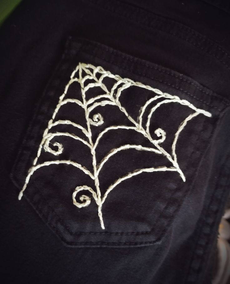 a spider web on the back of someone's black jean - pocket jeans with white stitching