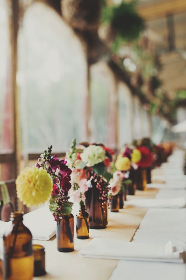 there are many vases that have flowers in them on the long table with paper