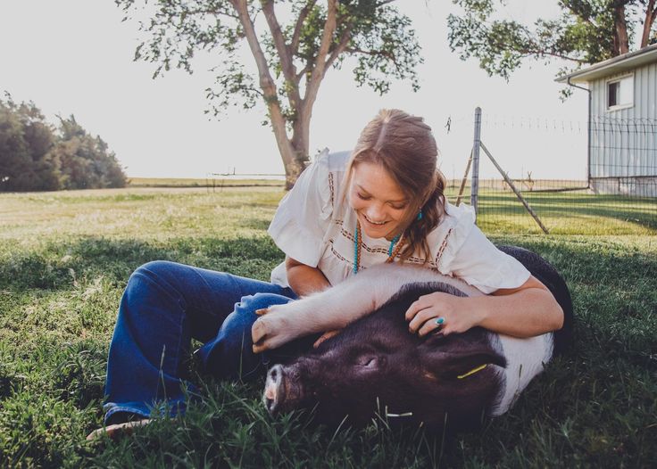 a woman is petting a pig in the grass