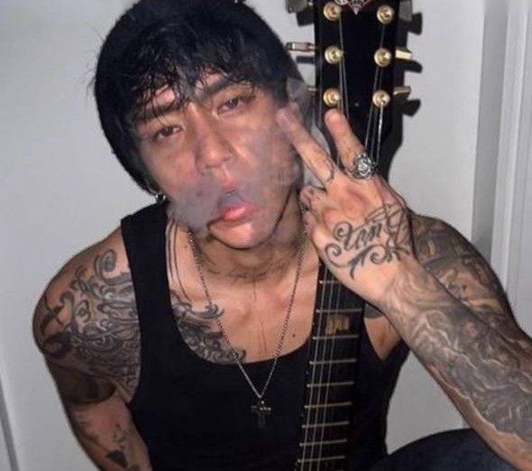 a man with black hair and tattoos holding his guitar up to his face while making a silly face