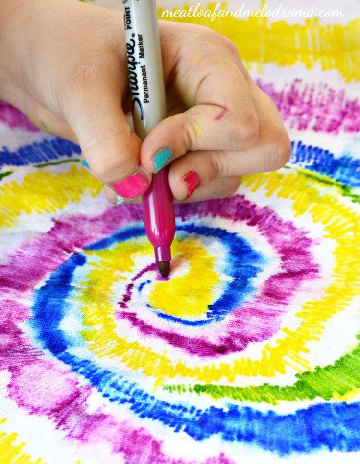 a woman is drawing on a colorful tie - dyed piece of paper with a marker