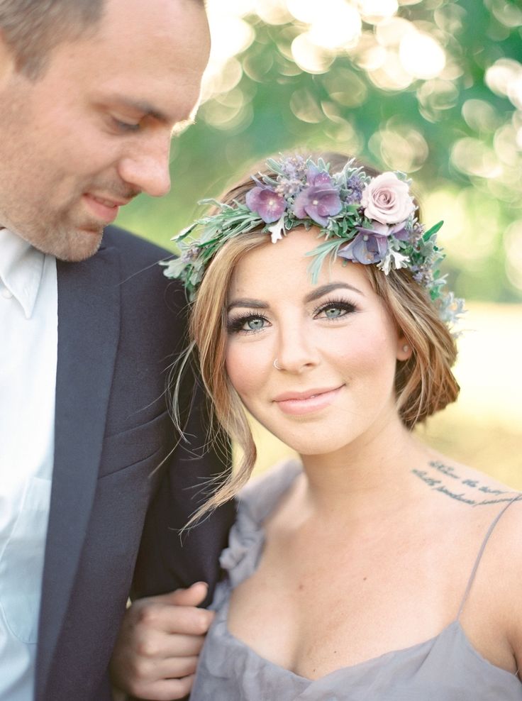 a man standing next to a woman wearing a flower crown on her head in front of trees