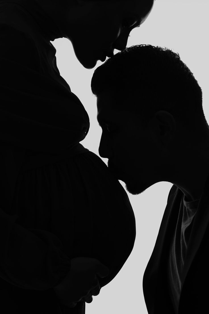 a pregnant couple kissing each other in silhouette