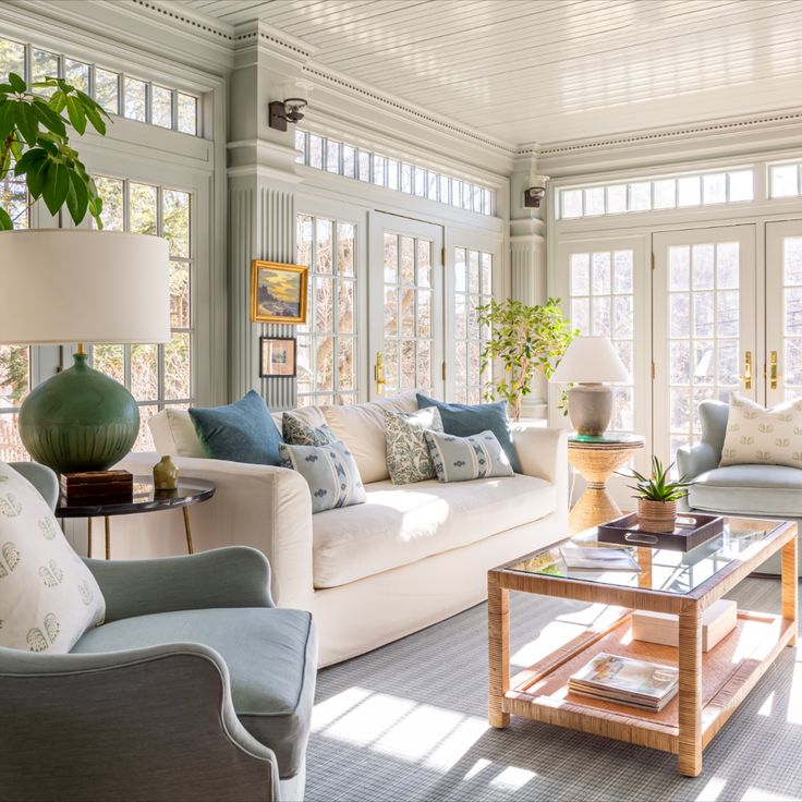 a living room filled with lots of furniture next to large window covered in sunlight shining through the windows