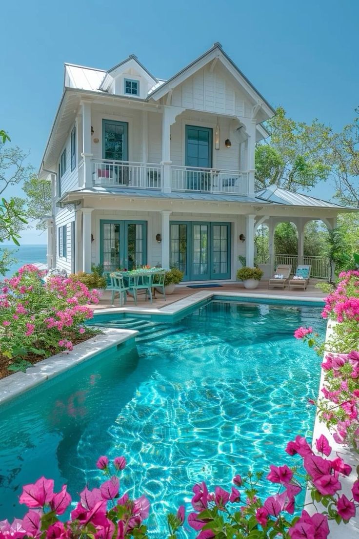 a house with a pool in front of it and pink flowers growing around the pool