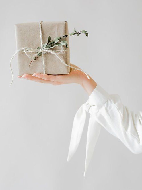 a woman's hand holding a wrapped present with greenery on it and tied in twine