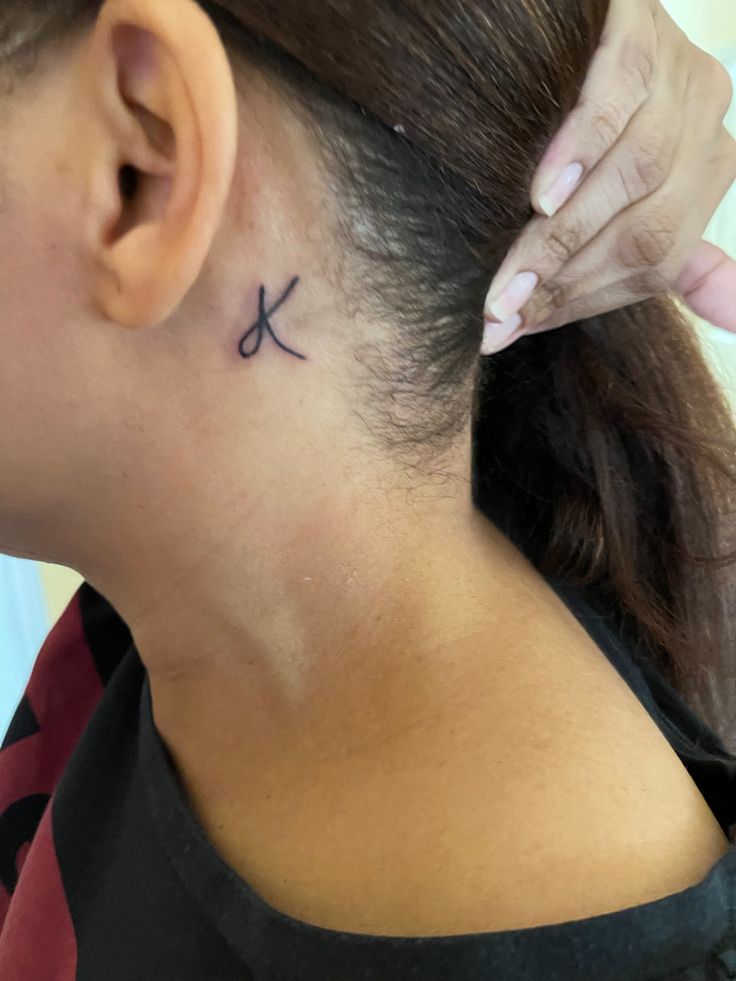 a woman with a small cross tattoo on her left side behind her ear, looking down at the ground