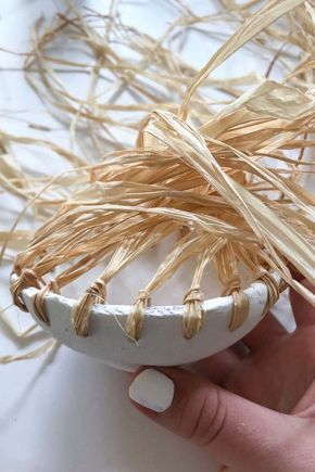 a hand holding a white bowl with dried grass in it