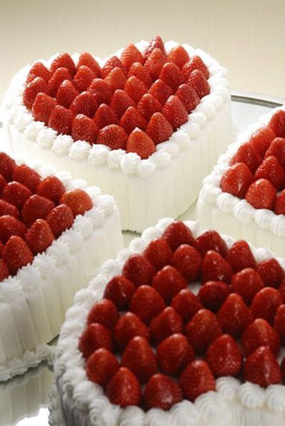 four cakes with strawberries arranged in the shape of hearts on a glass platter