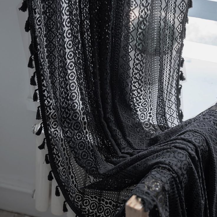 a black crocheted blanket sitting on top of a wooden table next to a window