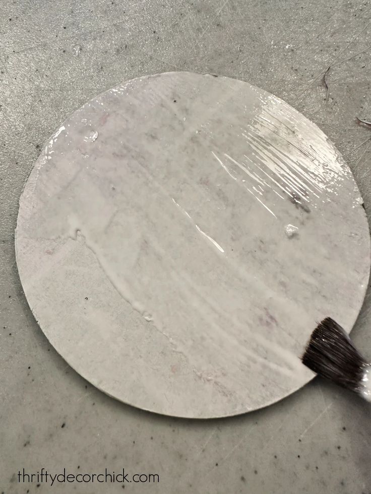 a paintbrush is sitting on the floor next to a round plate that has been painted white