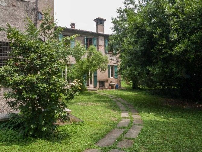 an old stone house in the middle of a grassy area with trees and bushes around it