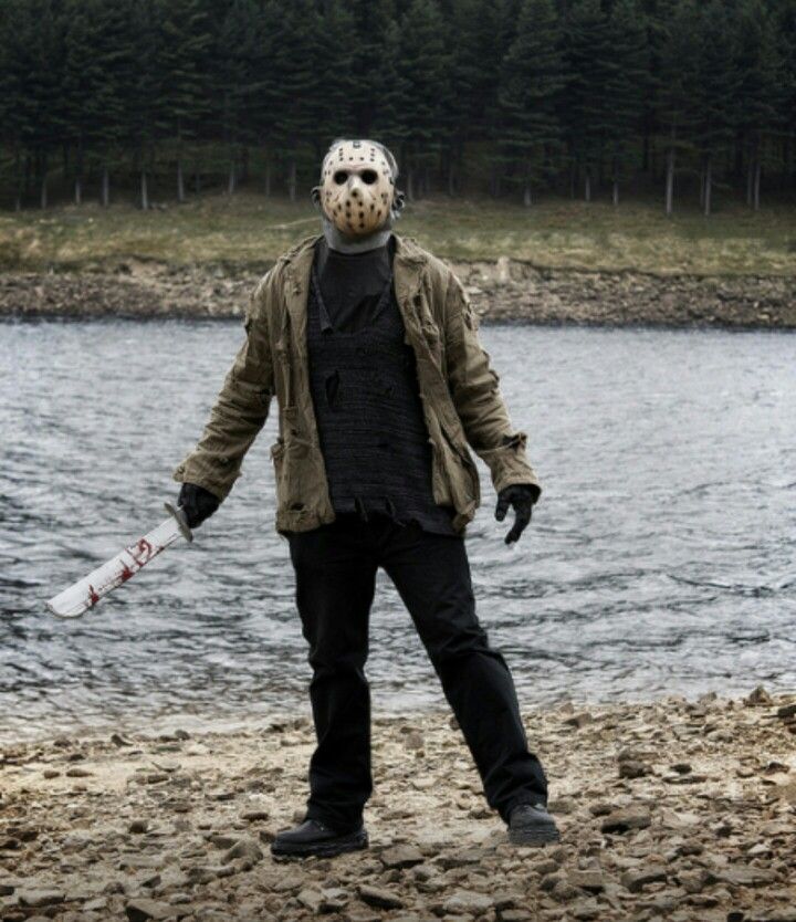 a man in a mask holding a baseball bat on the shore of a body of water